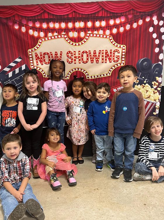 kids in front of a theater backdrop saying Now Showing